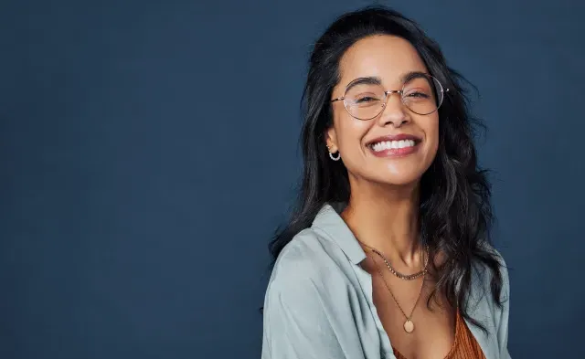 Beautiful university student having fun isolated against blue wall while wearing specs.